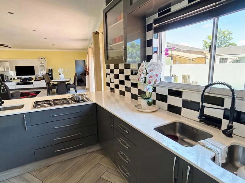 Modern open-plan kitchen featuring dark grey cabinetry, quartz countertops, a gas hob, and a distinctive checkered tile backsplash, flowing into the living area.