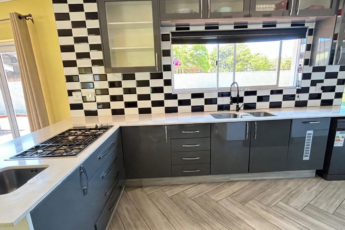 Modern kitchen featuring dark grey cabinetry, stone countertops, a gas hob, and a distinctive black and white checkered tile backsplash with herringbone flooring.