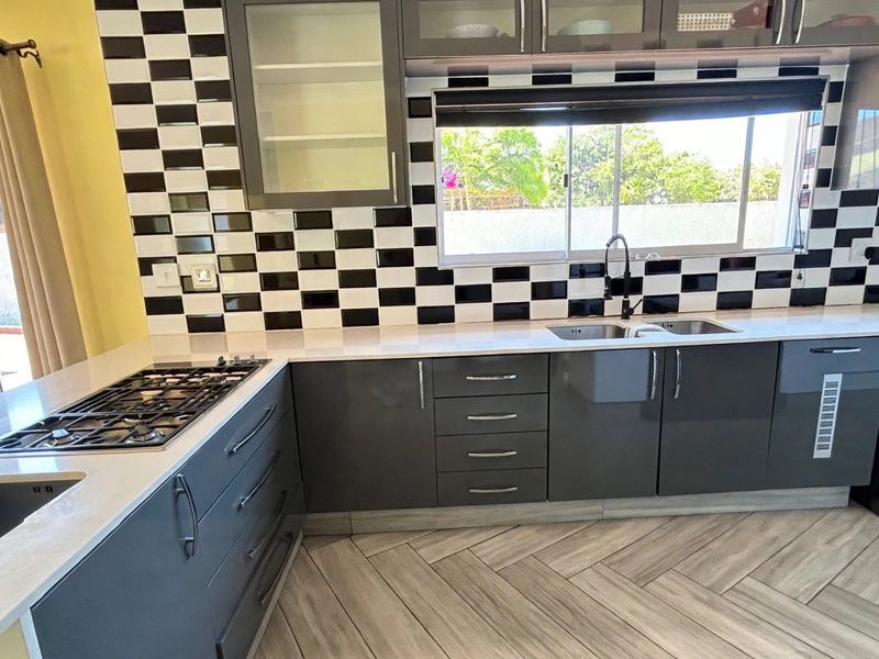 Modern kitchen featuring dark grey cabinetry, stone countertops, a gas hob, and a distinctive black and white checkered tile backsplash with herringbone flooring.