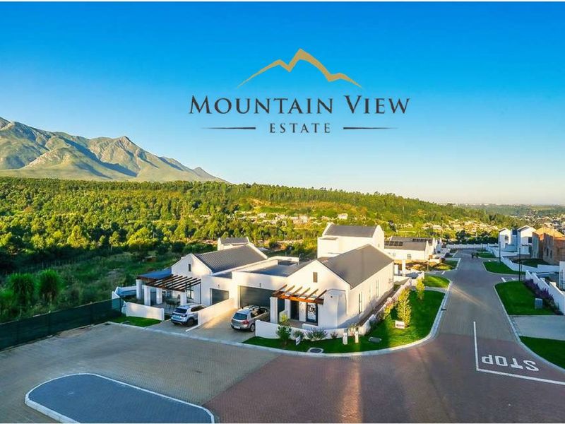 Aerial view of a modern residential estate featuring contemporary homes with pitched roofs, paved driveways, and scenic mountain views.