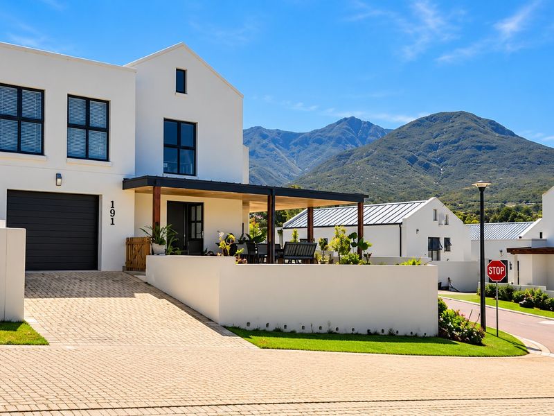 Modern two-story house with a paved driveway, integrated garage, and covered patio, set against a scenic mountain backdrop in a well-maintained estate.