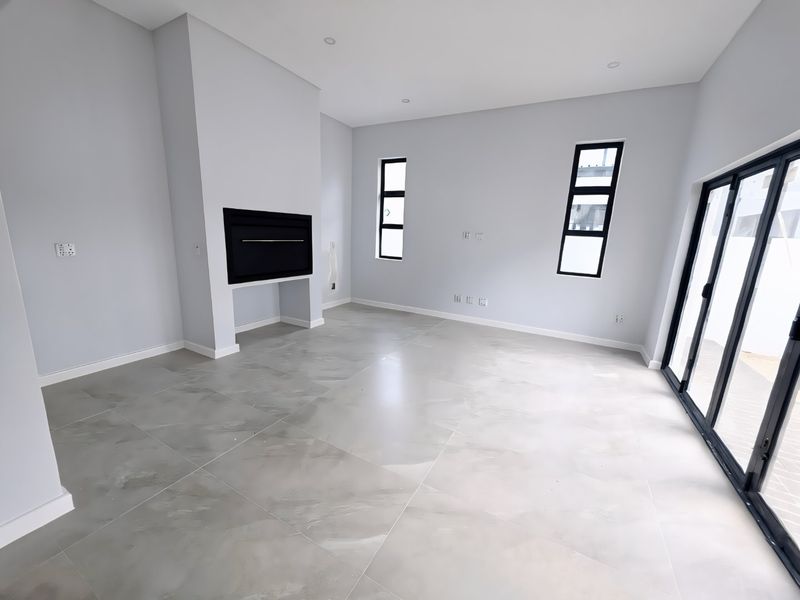 A bright, modern, and spacious living area featuring large format floor tiles, a built-in fireplace, and expansive sliding doors leading to the outdoors.
