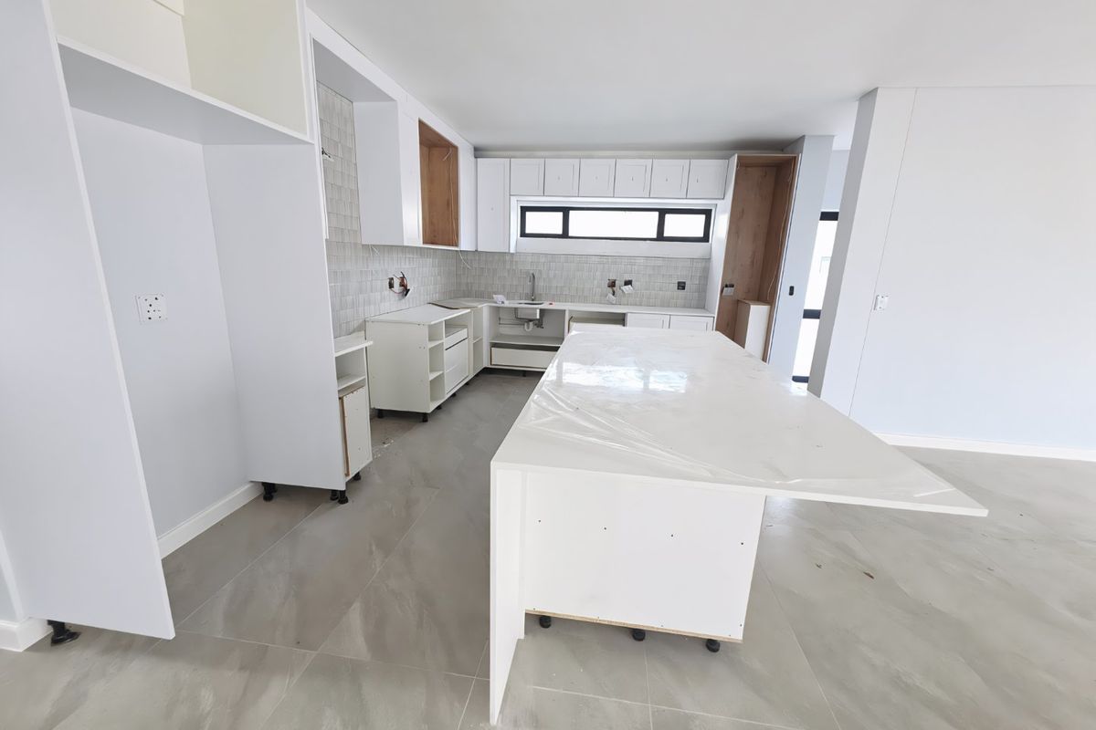 Modern kitchen under construction featuring a large central island, stone countertops, tiled backsplash, and ample built-in cabinetry, awaiting final installation and finishing touches.