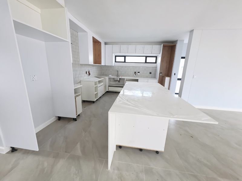 Modern kitchen under construction featuring a large central island, stone countertops, tiled backsplash, and ample built-in cabinetry, awaiting final installation and finishing touches.