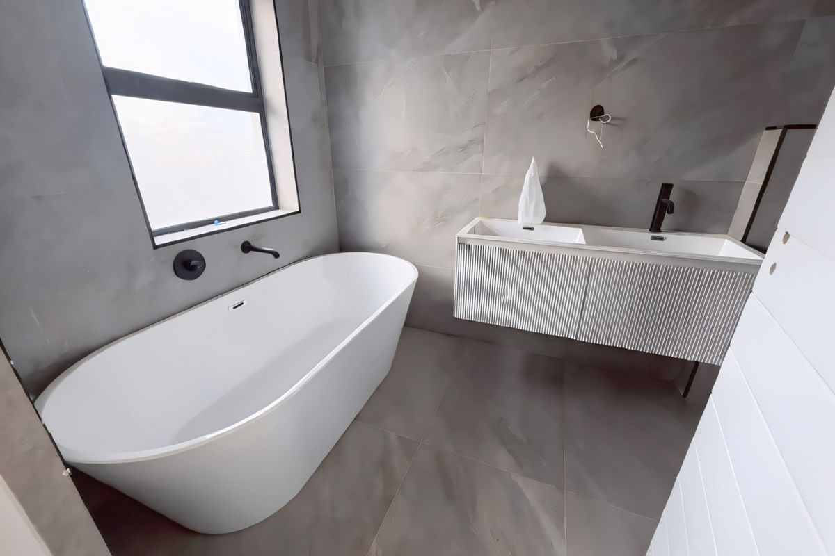 Modern bathroom featuring a sleek freestanding bathtub, double vanity with contemporary finishes, and large-format grey porcelain tiling throughout.