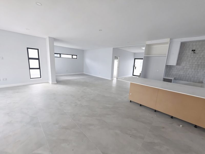Spacious open-plan living and kitchen area featuring modern tiled flooring, recessed lighting, and a central kitchen island with unfinished cabinetry.