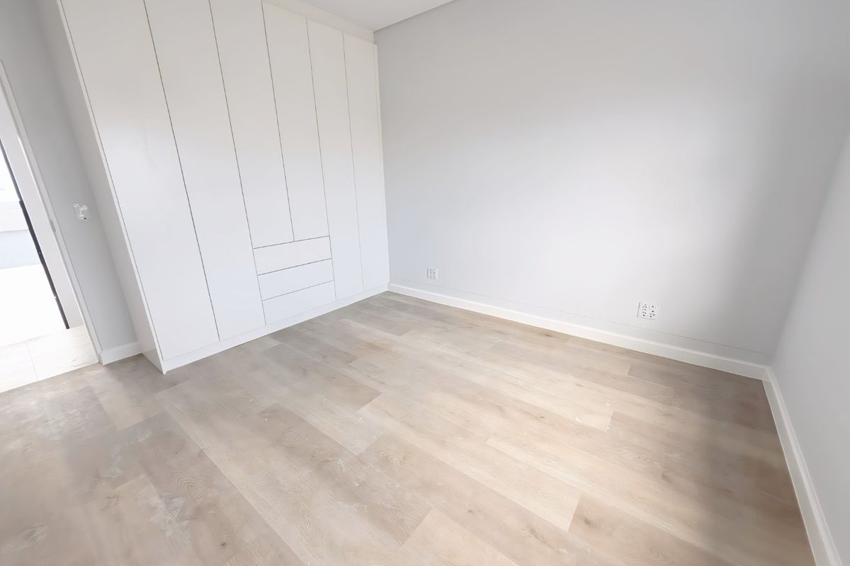 A bright, modern bedroom featuring neutral walls, light wood-look laminate flooring, and ample built-in cupboard storage.