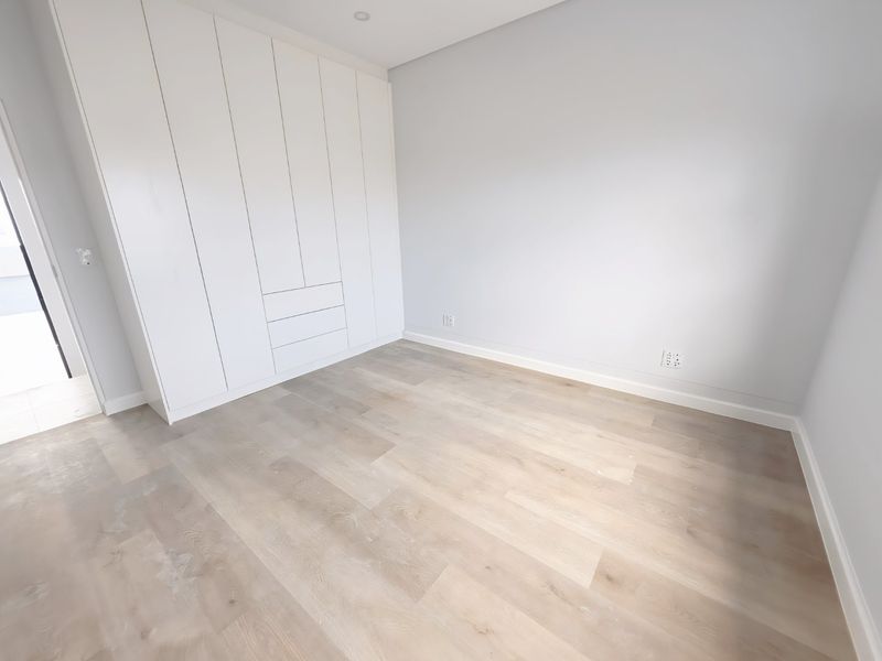 A bright, modern bedroom featuring neutral walls, light wood-look laminate flooring, and ample built-in cupboard storage.