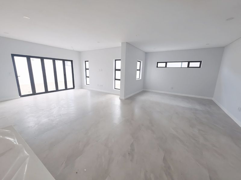 A spacious, modern open-plan living area featuring large format floor tiles, recessed lighting, and expansive aluminium stacker doors leading to the exterior.