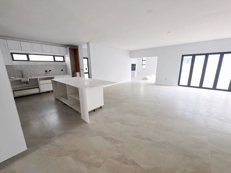 Spacious open-plan living and kitchen area featuring large format floor tiles, modern cabinetry, a central island, and expansive bi-fold doors leading outdoors.