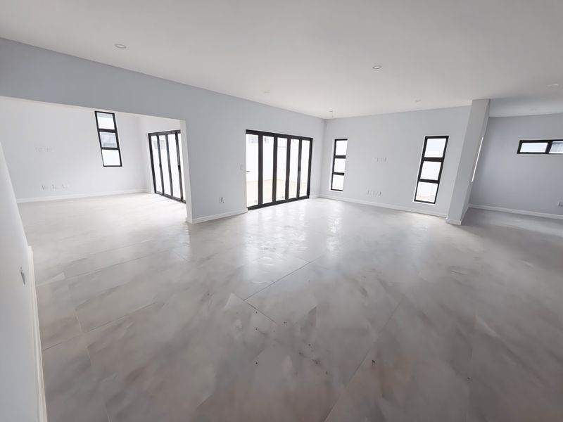 A spacious, modern open-plan living area featuring neutral finishes, large aluminium-framed windows, and sliding doors that provide ample natural light.