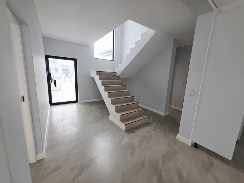 Modern, bright entrance hall featuring large format floor tiles, a contemporary staircase, and a glass-panelled front door leading to an open-plan interior.