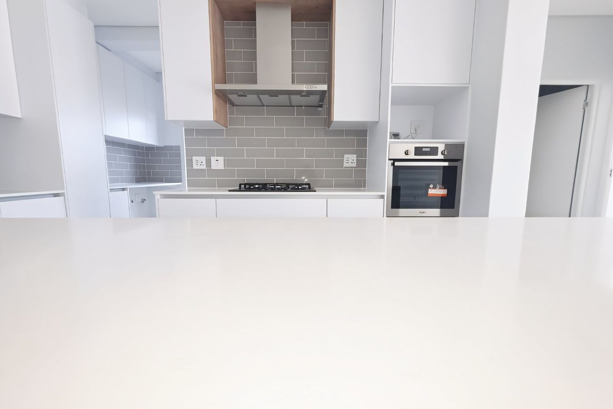 Modern kitchen featuring a clean white quartz island, subway tile backsplash, built-in oven, and gas hob with integrated extractor fan.