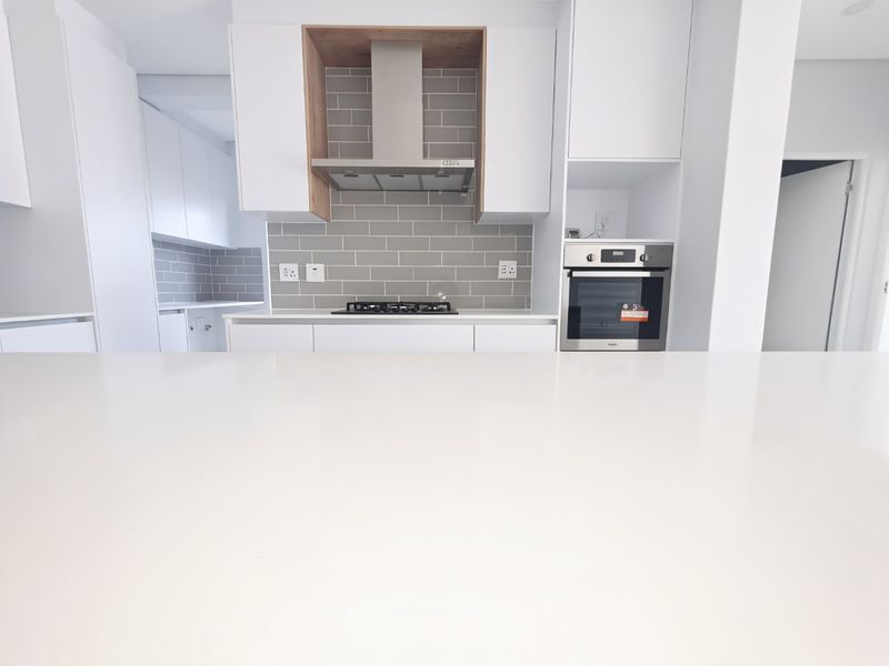 Modern kitchen featuring a clean white quartz island, subway tile backsplash, built-in oven, and gas hob with integrated extractor fan.