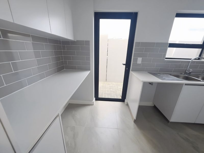 A modern, clean scullery featuring white cabinetry, grey subway tile backsplash, stainless steel sink, and direct access to an outdoor area.