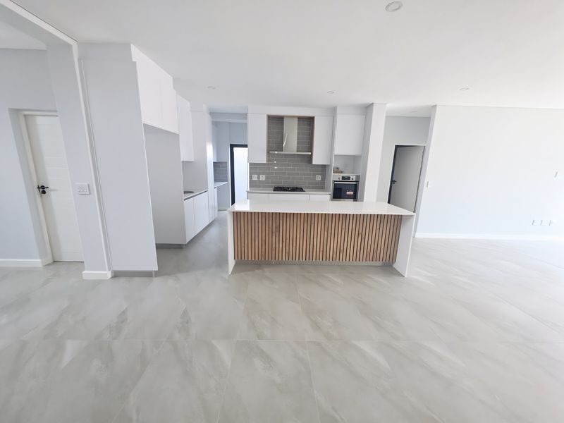 Modern open-plan kitchen featuring a central island with timber-slat detailing, sleek white cabinetry, subway tile backsplash, and high-quality porcelain floor tiles.
