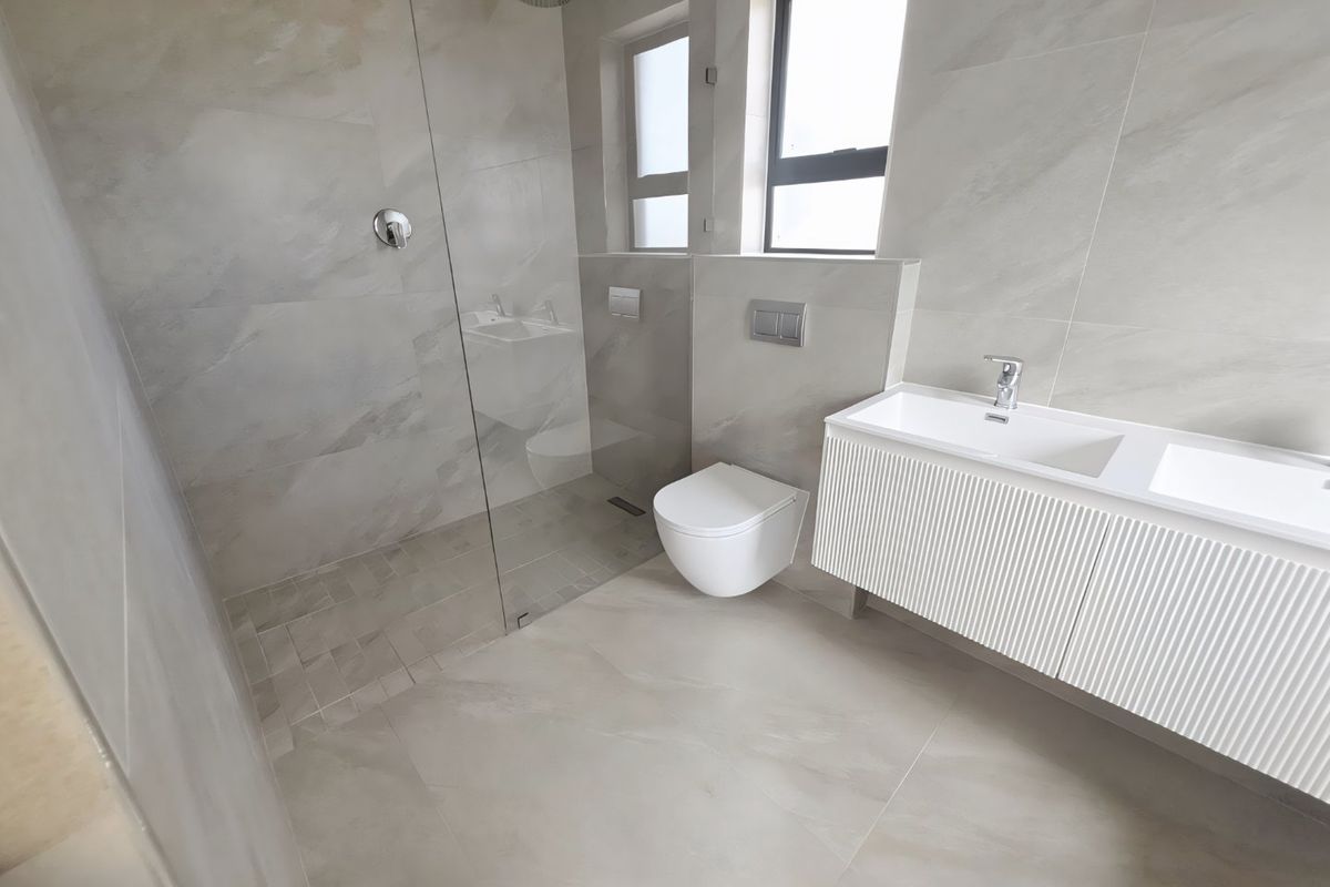 Modern bathroom featuring a walk-in shower with glass screen, wall-mounted toilet with concealed cistern, and a contemporary double vanity with integrated sinks.