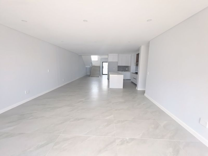 A spacious, modern open-plan living and kitchen area featuring large format floor tiles, recessed lighting, and a contemporary kitchen with a central island.