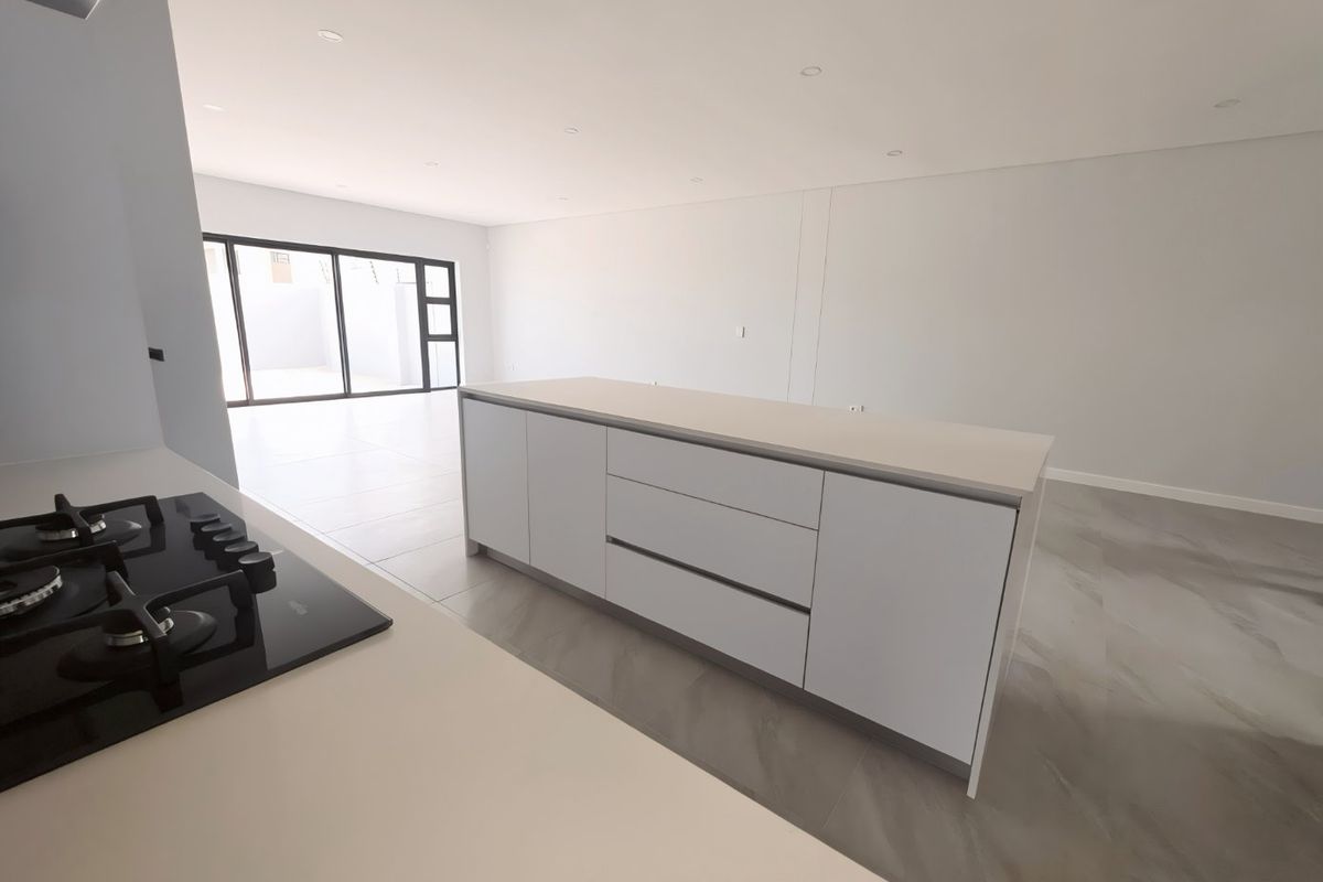 Modern open-plan kitchen and living area featuring a central island, gas hob, sleek cabinetry, and large sliding doors leading to an outdoor space.