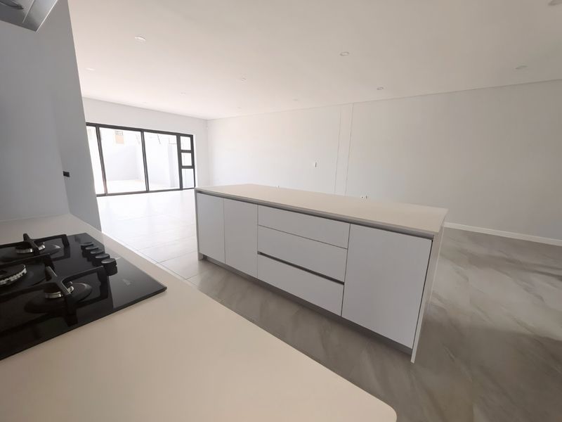 Modern open-plan kitchen and living area featuring a central island, gas hob, sleek cabinetry, and large sliding doors leading to an outdoor space.