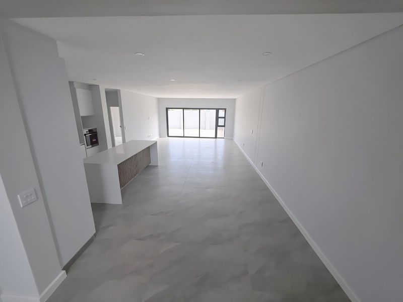 Spacious open-plan living and kitchen area featuring modern finishes, large format floor tiles, and seamless access to the outdoor space through sliding glass doors.