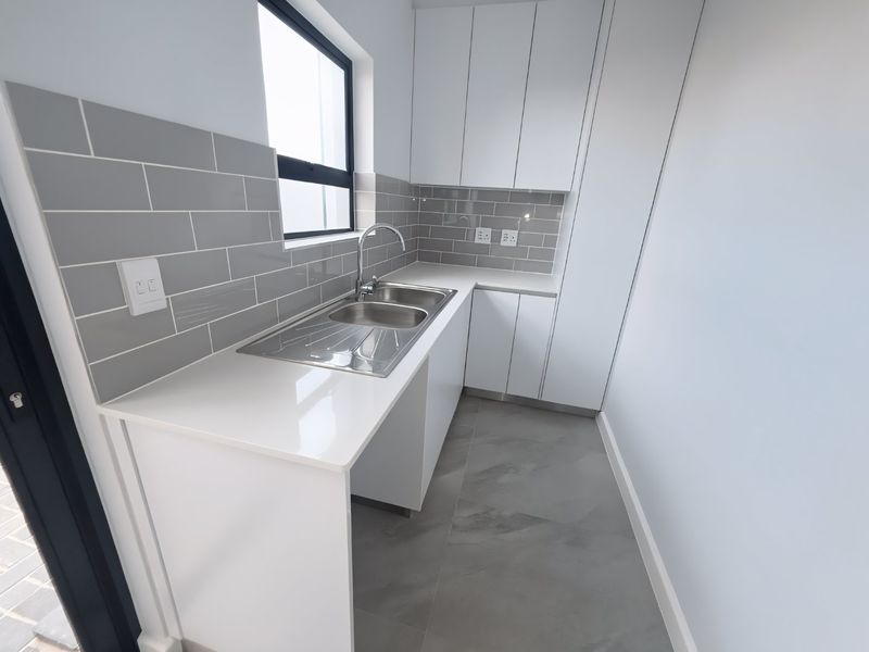 A modern, clean scullery featuring white cabinetry, quartz countertops, a stainless steel double sink, and grey subway tile backsplash.