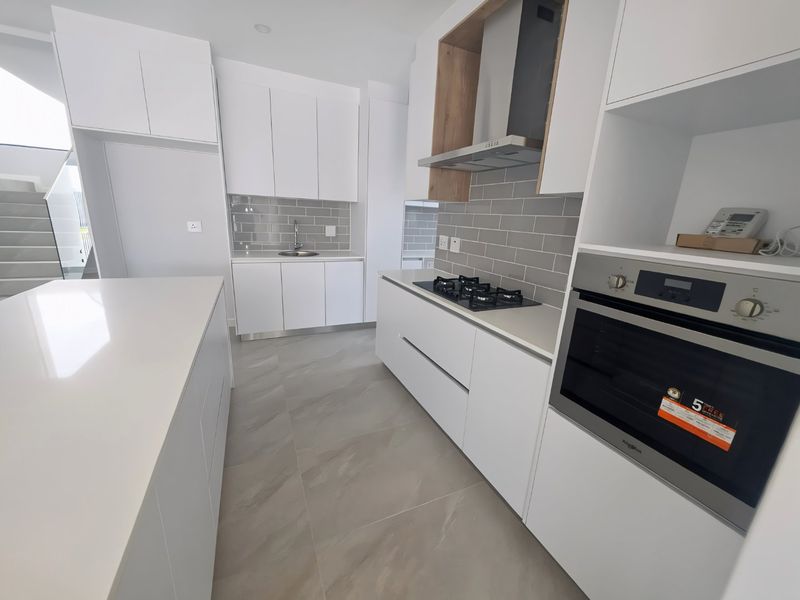 Modern kitchen featuring white cabinetry, stone countertops, a central island, gas hob, built-in oven, and a stylish grey subway tile backsplash.