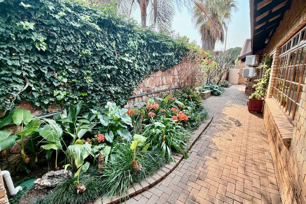 A well-maintained rear garden area featuring brick paving, a stone retaining wall with climbing ivy, and established garden beds along the townhouse exterior.