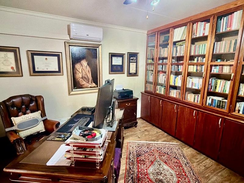 A dedicated home office featuring extensive built-in wooden cabinetry, wall-mounted air conditioning, and durable laminate flooring.