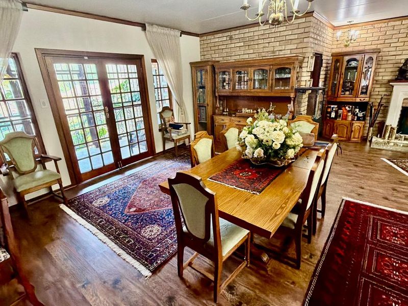 Spacious dining room featuring a brick fireplace, hardwood flooring, and double french doors providing access to the outdoor area.