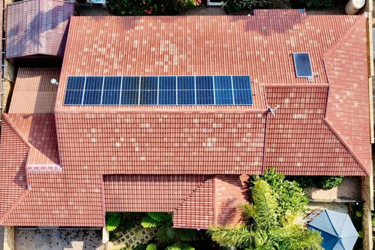 Aerial view of the townhouse property featuring a tiled roof with installed solar panels and solar geyser, surrounded by landscaped garden areas.