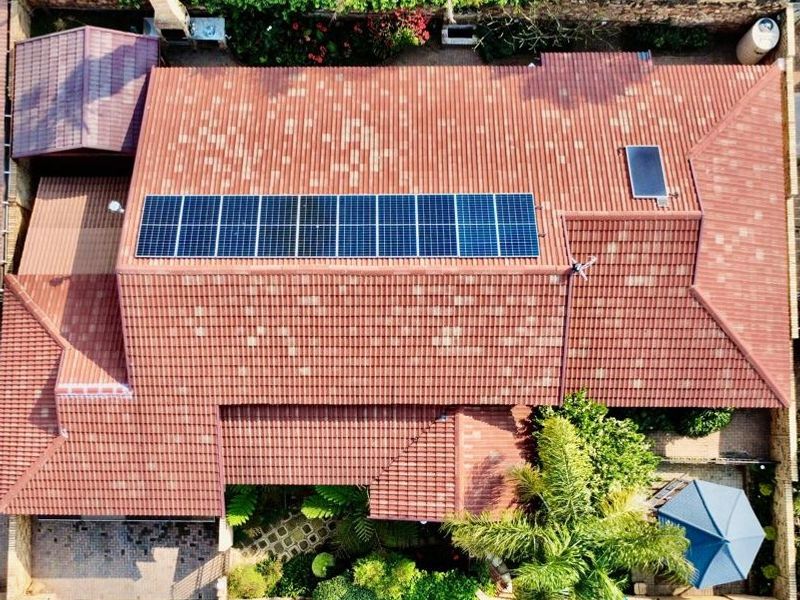 Aerial view of the townhouse property featuring a tiled roof with installed solar panels and solar geyser, surrounded by landscaped garden areas.