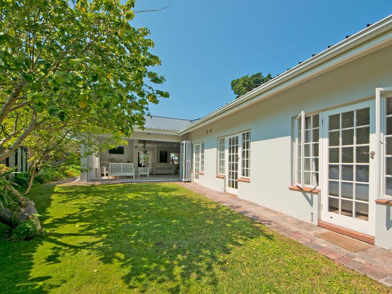 A well-maintained rear exterior view featuring a lush lawn, brick paved pathway, and multiple sets of french doors leading into the home.
