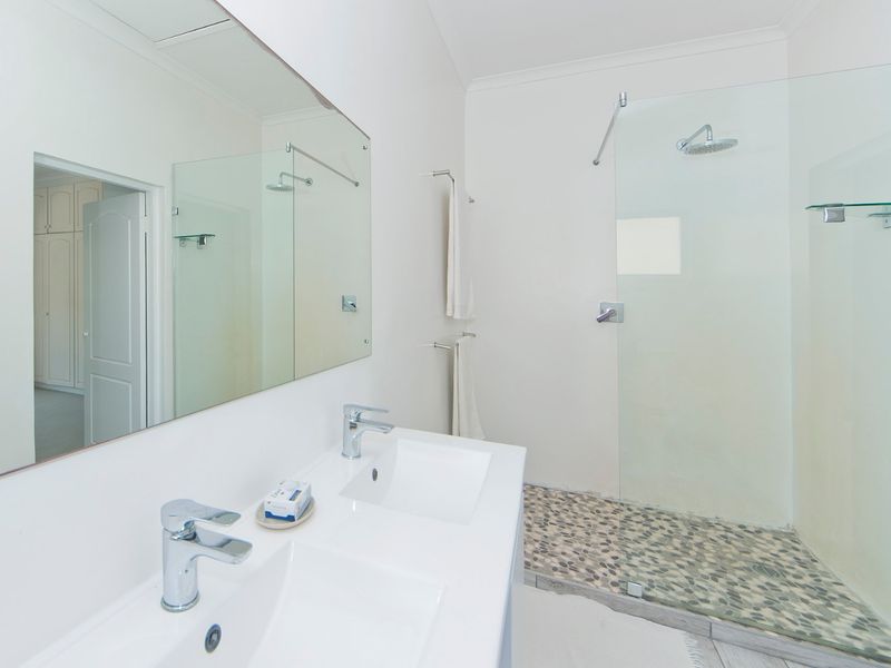Modern bathroom featuring a double vanity with chrome fixtures, a large wall mirror, and a spacious walk-in shower with a pebble tile floor.