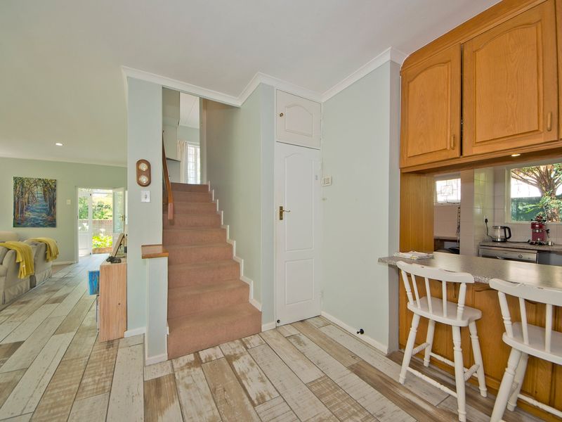 Open plan living area featuring a breakfast bar, wooden kitchen cabinetry, and a staircase leading to the upper level with light-toned laminate flooring.