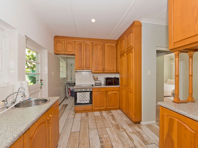 A functional kitchen featuring wooden cabinetry, laminate countertops, a built-in oven, and a stainless steel sink, with direct access to an adjacent scullery area.