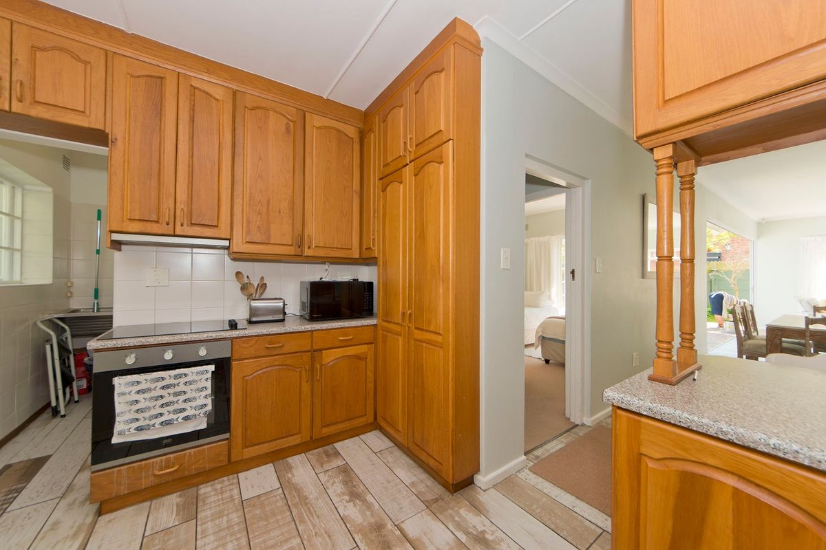 A functional kitchen featuring traditional timber cabinetry, laminate countertops, and built-in cooking appliances, with direct access to adjacent living and bedroom areas.