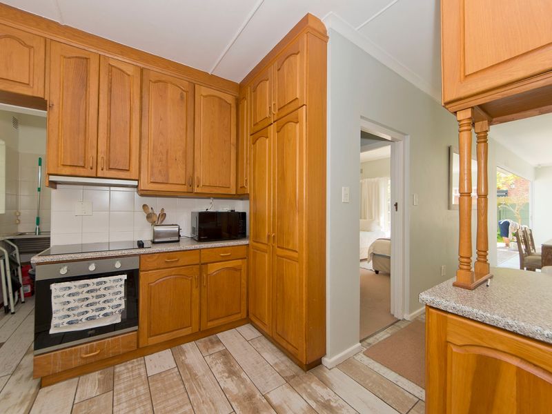 A functional kitchen featuring traditional timber cabinetry, laminate countertops, and built-in cooking appliances, with direct access to adjacent living and bedroom areas.