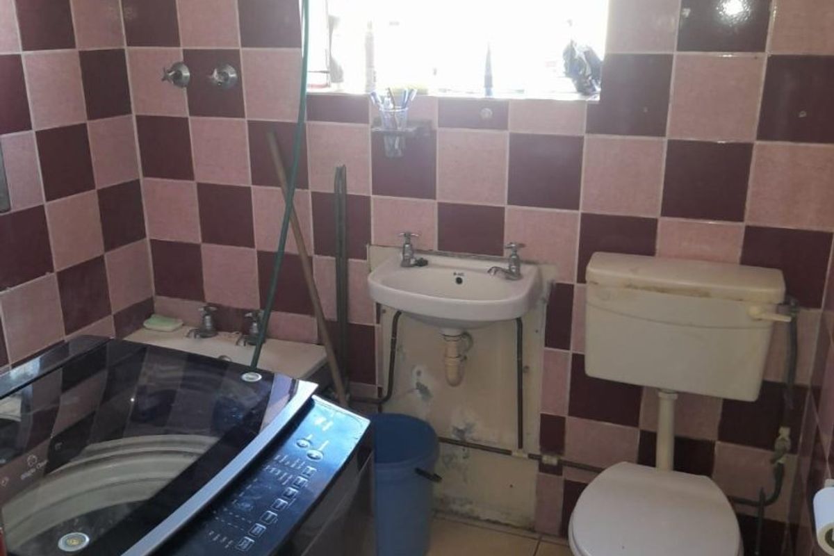 A dated bathroom featuring a wall-mounted basin, toilet, and shower head with checkered wall tiling and floor tiles.
