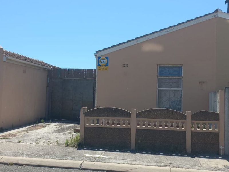 Front exterior view of the property featuring a concrete boundary fence, security gate, and paved driveway area.