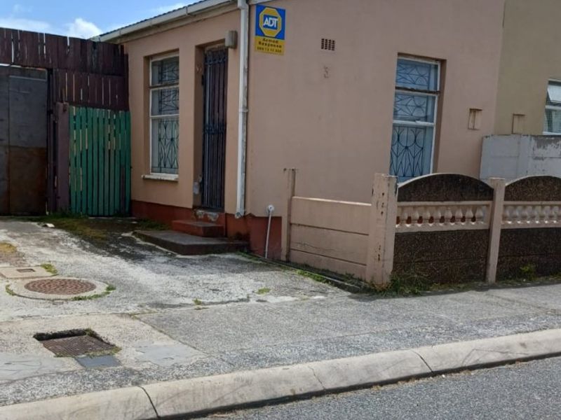 Front exterior view of a single-story house featuring a concrete driveway, security gate, and perimeter boundary wall.