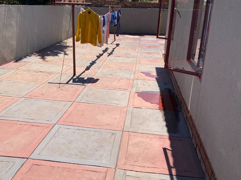 A rear exterior paved patio area featuring a boundary wall and access to the home via casement windows.