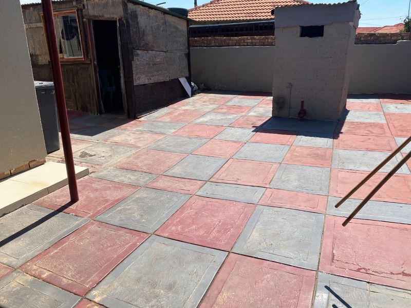 Rear outdoor area featuring a paved patio, boundary wall, and a detached outbuilding structure in need of maintenance.