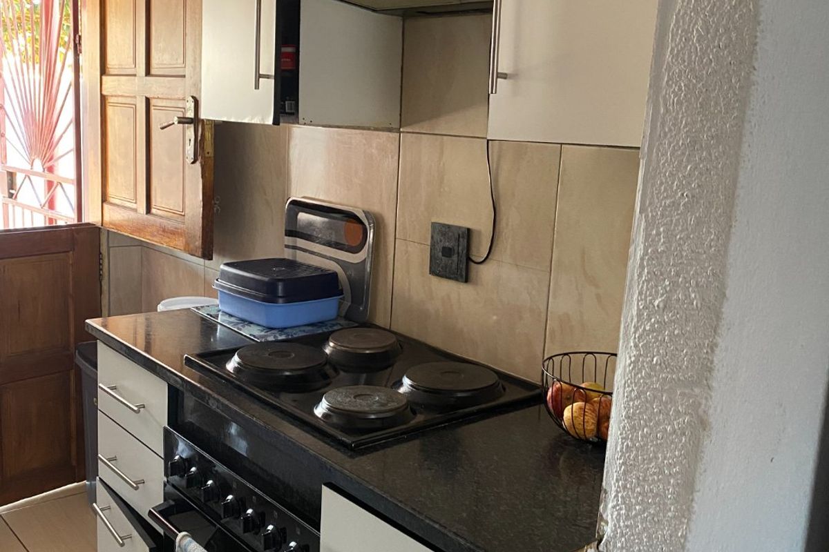 A compact kitchen featuring built-in cabinetry, a black electric hob with oven, extractor fan, and tiled backsplash.