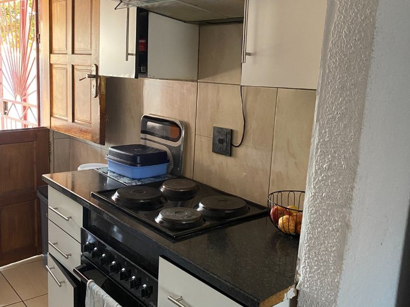 A compact kitchen featuring built-in cabinetry, a black electric hob with oven, extractor fan, and tiled backsplash.
