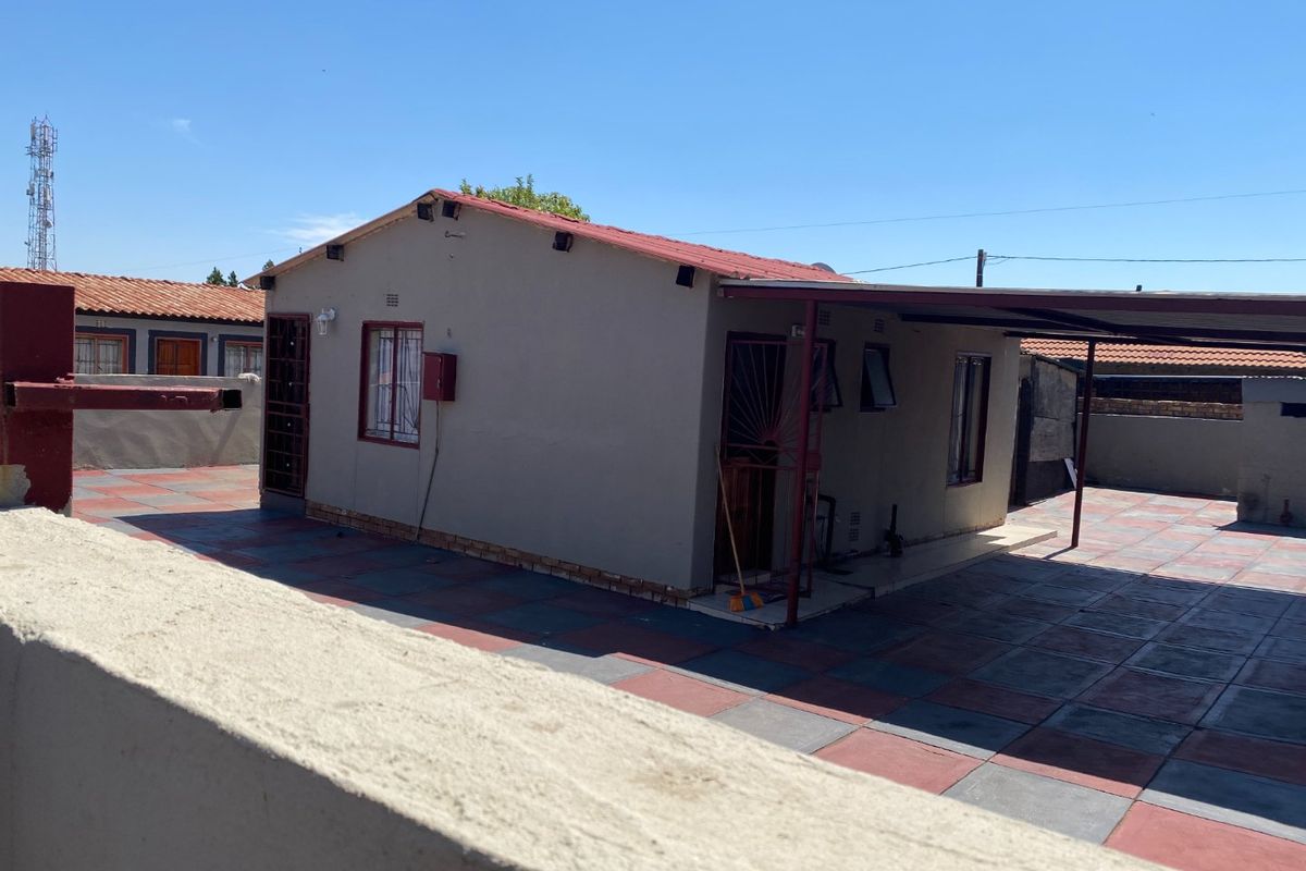 Rear view of the property featuring a paved patio area, a covered carport, and secure metal window bars.