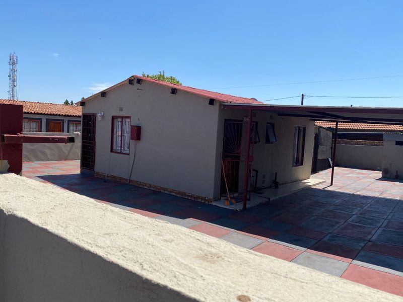 Rear view of the property featuring a paved patio area, a covered carport, and secure metal window bars.