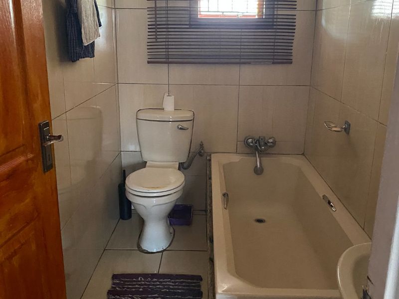 A compact bathroom featuring a standard bathtub, toilet, and full-height wall tiling. The space would benefit from modern updates to fixtures and finishes.