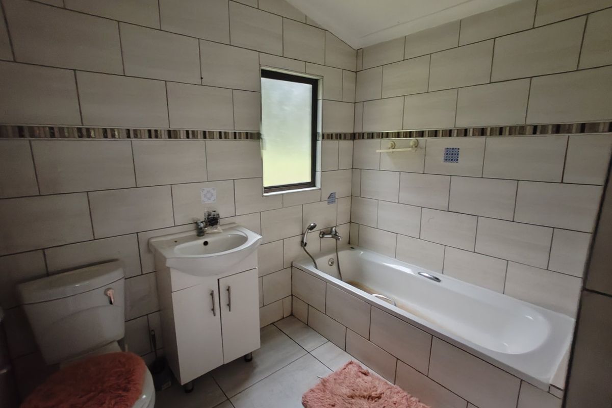 A functional bathroom featuring full-height wall tiling, a built-in vanity with basin, a standard bathtub, and a toilet.