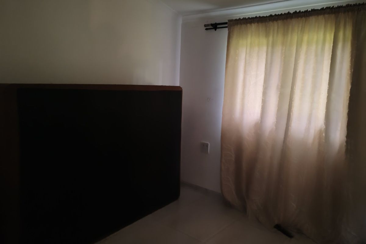 A simple, empty bedroom featuring tiled flooring and a window with a curtain rod, offering a blank canvas for personalization.
